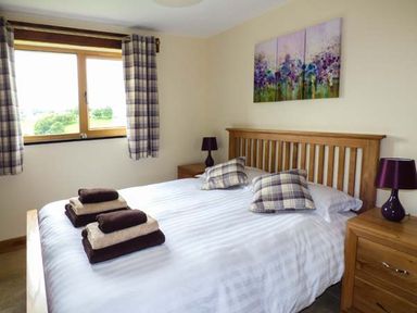 A bedroom with a double bed pillows and folded towels on the bed bedside tables with lamps and checkered curtains at Tyn Y Celyn Uchaf in Clocaenog near Ruthin