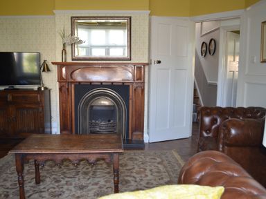 A living room with a wooden fireplace centered below a mirror and a wooden table in front at Lily House in Minehead