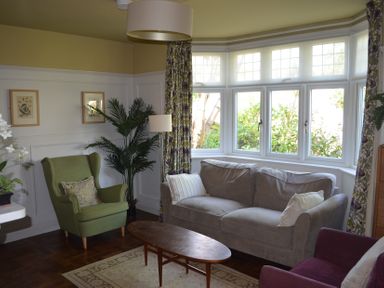 A living room with a large window a gray sofa a green armchair a purple chair and a wooden coffee table at Lily House in Minehead