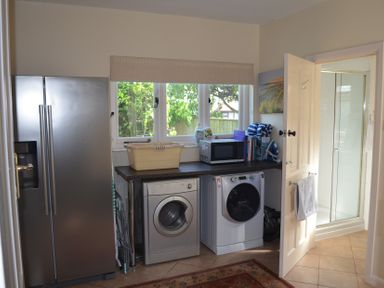 A laundry room with a refrigerator washing machine dryer microwave and cleaning supplies at Lily House in Minehead