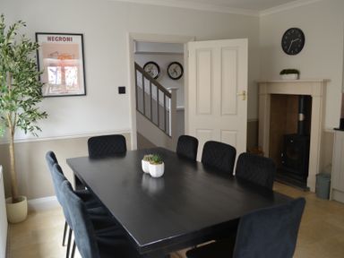 A dining room with a black table and chairs a potted plant on the table a fireplace a wall clock and a framed picture at Lily House in Minehead