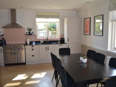 A kitchen with white cabinets black countertop a stainless steel oven a dining table with black chairs and framed pictures on the wall at Lily House in Minehead