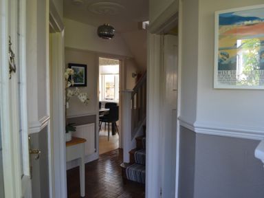 A hallway with a small table and white orchid leading to a dining room and staircase at Lily House in Minehead