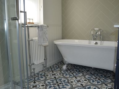 A bathroom with a white clawfoot bathtub a patterned tile floor a towel hanging on a chrome radiator and a shower enclosure at Lily House in Minehead