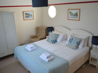 A bedroom with a double bed with blue and white pillows and towels on the bed a beige armchair a white wardrobe and nightstands with blue lamps at Lily House in Minehead