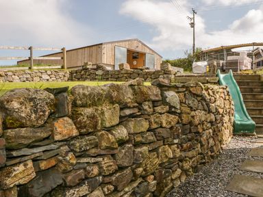 An outdoor area with a stone wall steps green slide and wooden barn at Higher Whiddon Farm Whiddon Well Ashburton near Newton Abbot