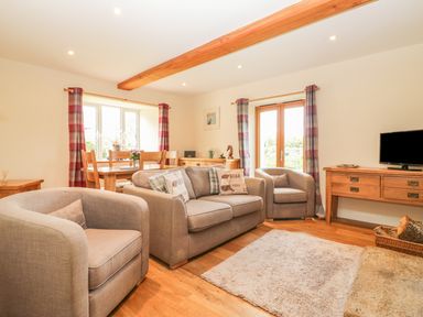 A living room with grey sofas and a wooden dining table near windows with checkered curtains at Higher Whiddon Farm Whiddon Well Ashburton near Newton Abbot