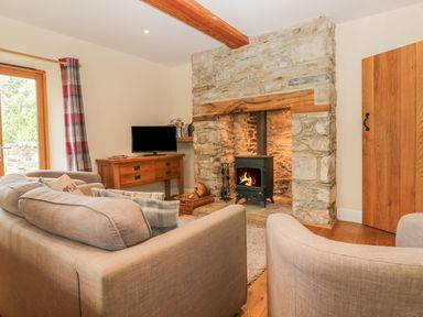 A living room with a stone fireplace, wood-burning stove, wooden furniture, and beige sofas at Higher Whiddon Farm Whiddon Well Ashburton near Newton Abbot