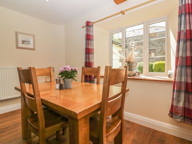 A dining area with a wooden table and chairs a plant and salt and pepper shakers on the table red and gray plaid curtains at a window at Higher Whiddon Farm Whiddon Well Ashburton near Newton Abbot