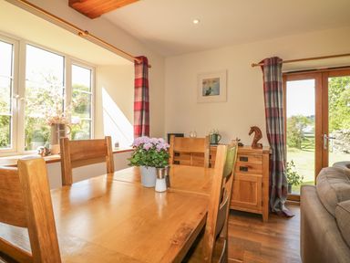 A dining area with wooden table and chairs next to large window and wooden cabinet with decorative items at Higher Whiddon Farm Whiddon Well Ashburton near Newton Abbot
