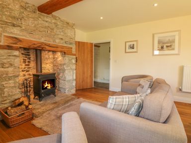 A living room with a stone fireplace wood burning stove and beige sofas at Higher Whiddon Farm Whiddon Well Ashburton near Newton Abbot