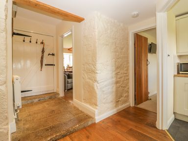 A hallway with wooden floors a white wooden door and two doorways leading to other rooms at Higher Whiddon Farm Whiddon Well Ashburton near Newton Abbot