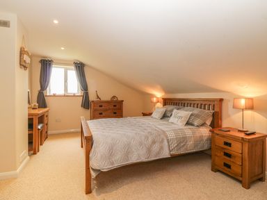A bedroom with a wooden bed table and dresser near a window with curtains at Higher Whiddon Farm Whiddon Well Ashburton near Newton Abbot