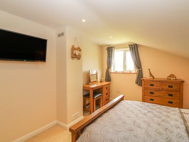 A bedroom with a wall-mounted TV a wooden dressing table under a window and a wooden chest of drawers at Higher Whiddon Farm Whiddon Well Ashburton near Newton Abbot