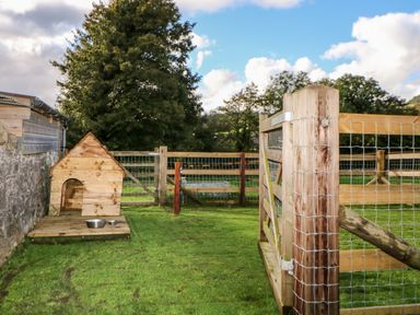 A fenced outdoor area with a wooden dog house and two metal bowls on grass at Higher Whiddon Farm Whiddon Well Ashburton near Newton Abbot