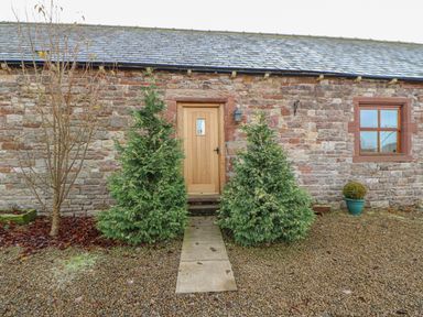A stone building with wooden door and window with a pathway and shrubs at Swift Cottage in Milton near Brampton
