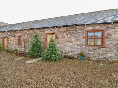 A stone building with a wooden door two windows and small trees in front at Swift Cottage in Milton near Brampton