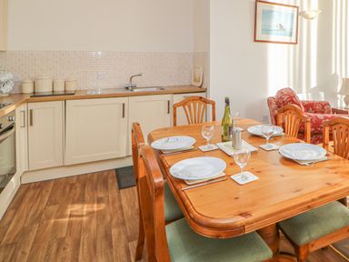 A kitchen with wooden dining table set with plates glasses and a bottle near a sitting area with red patterned armchair at Swift Cottage in Milton near Brampton
