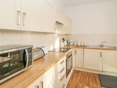 A kitchen with cream cabinets wooden countertops a microwave bread bin oven stovetop kettle canisters and a sink at Swift Cottage in Milton near Brampton