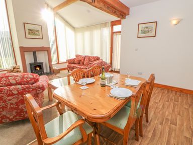A dining area with a wooden table set for four and a living area with two patterned sofas and a fireplace at Swift Cottage in Milton near Brampton