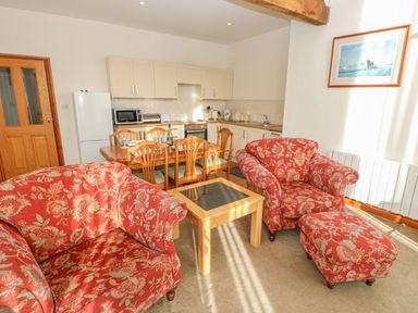 A living area with two patterned armchairs and an ottoman a wooden coffee table and a dining table with chairs in a kitchen at Swift Cottage in Milton near Brampton