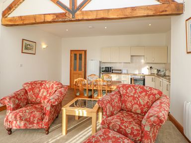 A living area with red floral armchairs a wooden coffee table and a dining table with chairs in an open kitchen space at Swift Cottage in Milton near Brampton