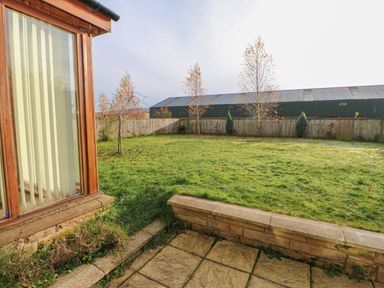 A garden with grass trees and a wooden fence outside a house with large windows at Swift Cottage in Milton near Brampton