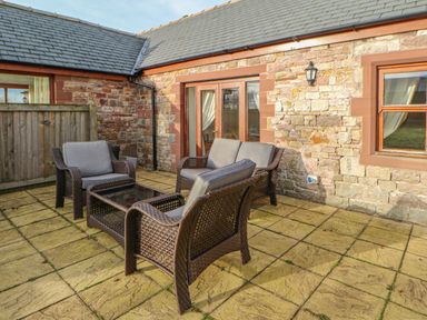An outdoor patio with wicker furniture including chairs and a table outside a stone building at Swift Cottage in Milton near Brampton