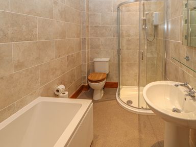 A bathroom with a bathtub toilet with wooden seat glass shower and pedestal sink at Swift Cottage in Milton near Brampton