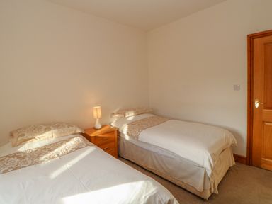 A bedroom with two single beds a nightstand with a lamp and a wooden door at Swift Cottage in Milton near Brampton