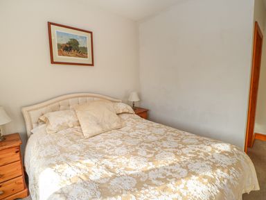 A bedroom with a double bed with patterned bedding two bedside tables with lamps and a framed painting on the wall at Swift Cottage in Milton near Brampton