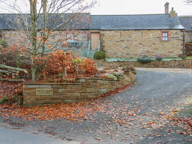 A driveway with fallen leaves and stone wall with a sign reading Milton Mains Cottages next to a stone building at Swift Cottage in Milton near Brampton