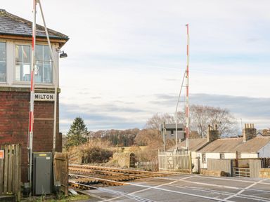 A railway level crossing with barriers and a signal box labeled Milton near houses and trees at Swift Cottage in Milton near Brampton