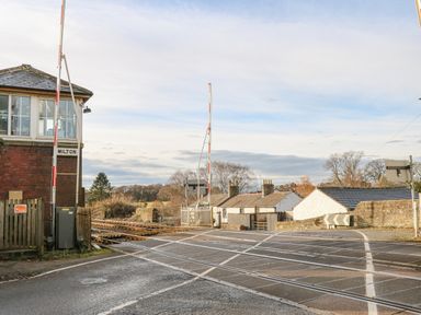 A level railway crossing with barriers and a signal box next to a road at Swift Cottage in Milton near Brampton