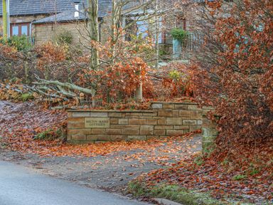 An entrance driveway with fallen leaves and stone wall with a sign saying Milton Mains Cottages with stone cottages in the background at Swift Cottage Milton near Brampton
