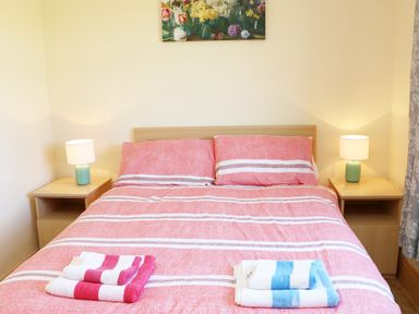 A bedroom with a double bed with red striped bedding two bedside tables with lamps and folded towels on the bed at Clash-Brack in Dungarvan County Waterford