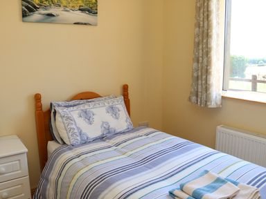 A bedroom with a wooden bed with striped bedding and a small white bedside table at Clash-Brack in Dungarvan County Waterford