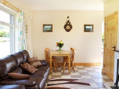 A living room with a brown leather sofa pillows a wooden dining table with four chairs and a vase of flowers on it at Clash-Brack in Dungarvan County Waterford