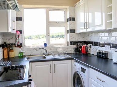 A kitchen with white cabinets a black countertop a sink a washing machine a red kettle and a window showing trees at Clash-Brack in Dungarvan County Waterford