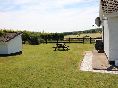 A backyard with a picnic table a small shed and a fenced grassy area with hay bales in the distance at Clash-Brack in Dungarvan County Waterford