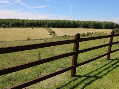 A wooden fence overlooking hay bales in a field with trees in the background at Clash-Brack in Dungarvan County Waterford