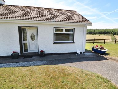 Front view of a house with a white door and window two flower pots near the door and a blue flower planter on the right side at Clash-Brack in Dungarvan County Waterford