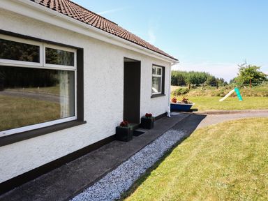 An exterior view of a white house with two windows and a small entrance surrounded by grass and a garden with a slide at Clash-Brack in Dungarvan County Waterford