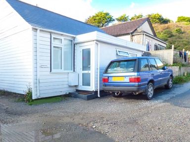 A blue car parked next to a white house with a small porch and window at Tidewood in Polzeath