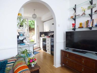 A living room with a colorful striped blanket on a sofa a wooden cabinet with a television and shelves with books and decor at Tidewood in Polzeath
