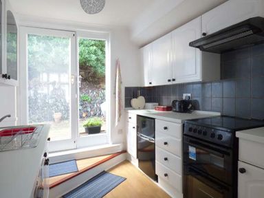 A kitchen with white cabinets black appliances and glass doors leading outside at Tidewood in Polzeath