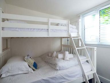 A bunk bed with white bedding and folded towels near a window with blinds at Tidewood Polzeath