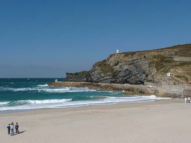 A sandy beach with waves and a rocky cliff with a small lighthouse at Tidewood in Polzeath