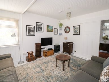 A living room with two sofas a round wooden table and a wall mounted TV at Driftwood in Polzeath near Wadebridge