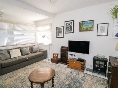 A living room with a sofa table lamp wooden coffee table television and wall art at Driftwood Polzeath near Wadebridge